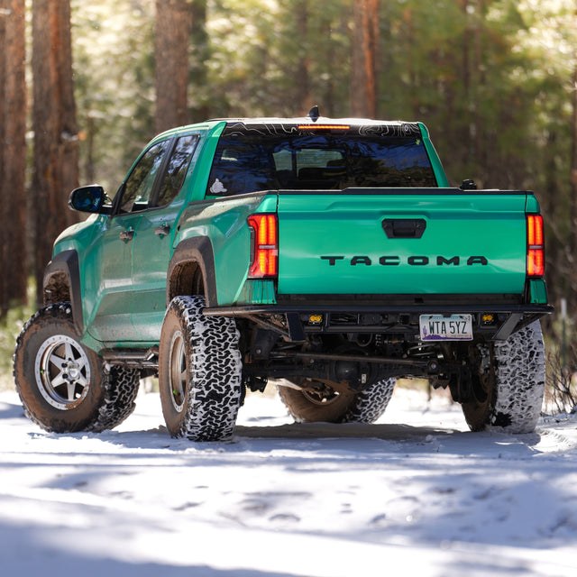 Green 4th Gen Toyota Tacoma rear view with DRT High Clearance Rear Bumper on a snowy forest road