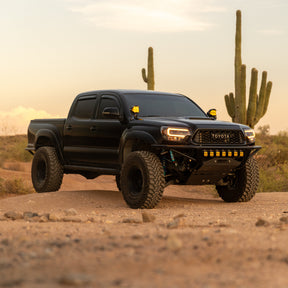 Black 2nd Gen Toyota Tacoma with DRT Crossmember Delete Front Bumper and amber lights in saguaro desert at dusk